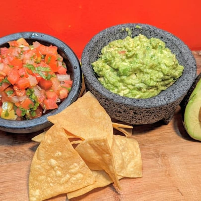 Pico de gallo and guacamole in molcajete bowls with tortilla chips and a halved avocado.